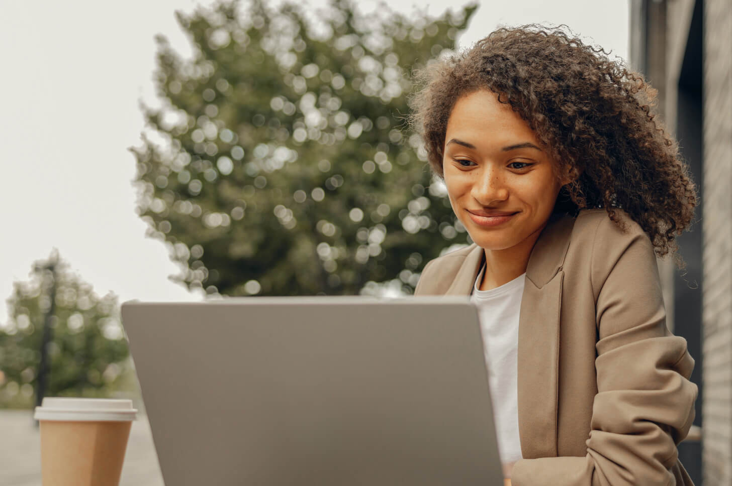 Lady sat outside in front of a laptop with a cup of coffee alongside