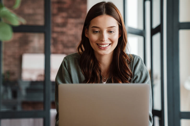 Woman sat in front of a laptop working while smiling